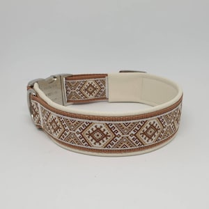 Könnte beinhalten: Ein weißes Lederhundekragen mit einem braunen und weißen geometrischen Muster. Das Halsband hat eine silberne Schnalle und einen D-Ring.