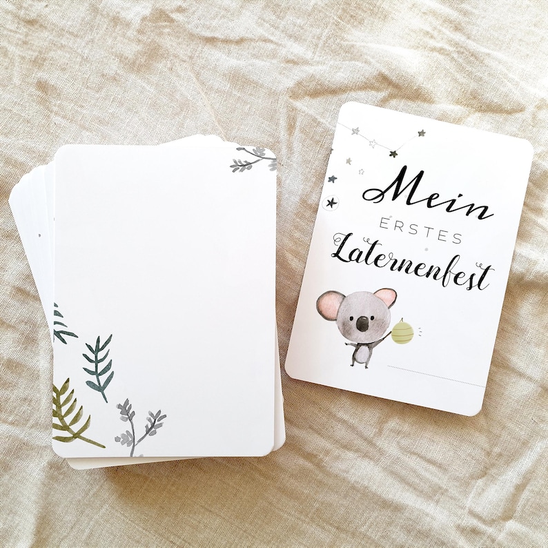 May include: A white card with a koala holding a lantern. The card says "Mein erstes Laternenfest" which translates to "My first lantern festival".