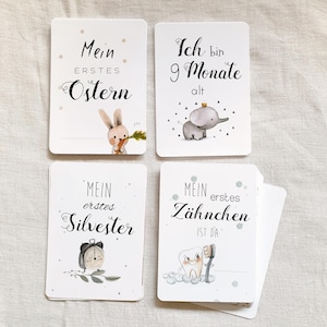 May include: Four white cards with black text and illustrations. The cards feature milestones for a baby, such as "My First Easter", "My First Tooth", "My First New Year's Eve", and "I am 9 months old".