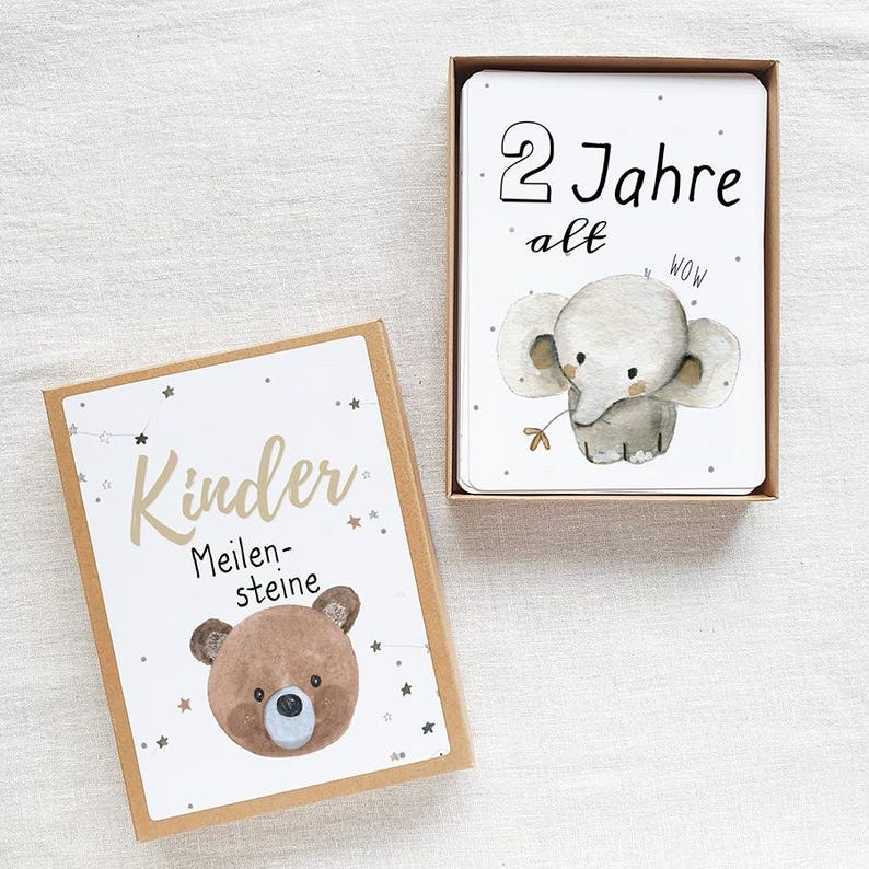May include: A set of milestone cards for children. The cards feature a brown bear and an elephant with the text "Kinder Meilensteine" and "2 Jahre alt".