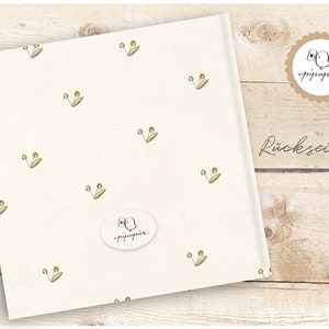 May include: A white card with a repeating pattern of small green leaves and yellow dots. The card has a white oval sticker with a small bird illustration and the text "pippapier" in black. The text "R&uuml;ckseite" is printed in black on a wooden surface.