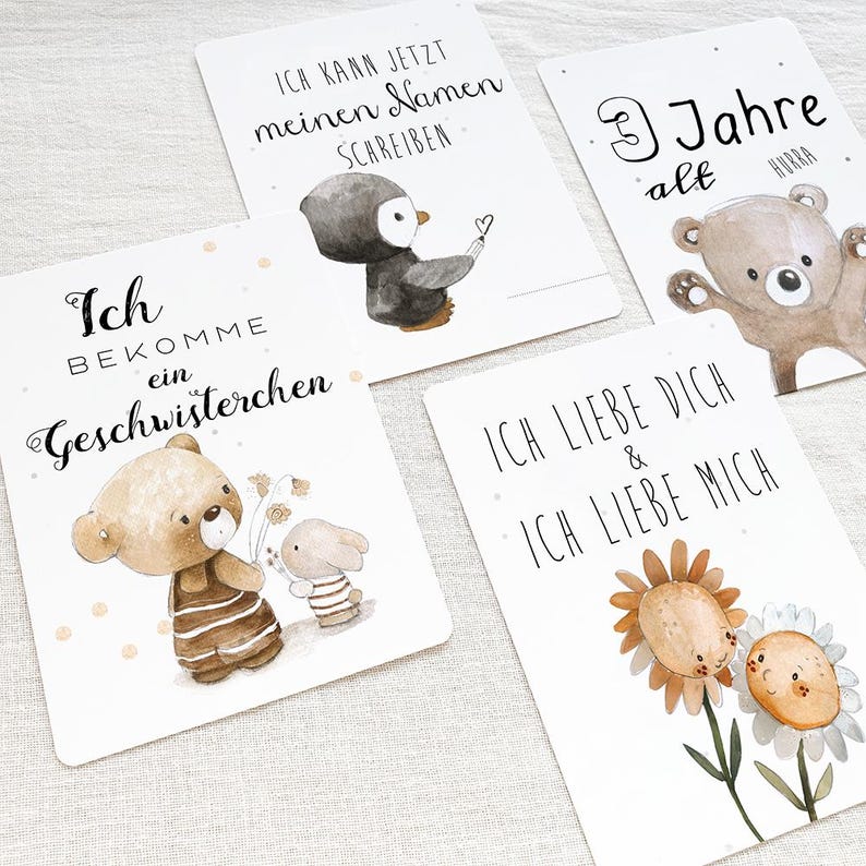 May include: Four illustrated cards with different messages. The first card features a brown bear holding flowers and a bunny rabbit. The text reads "I am getting a sibling". The second card features a penguin writing its name. The text reads "I can write my name now". The third card features a brown bear with the text "3 years old hooray". The fourth card features two sunflowers with the text "I love you and I love myself".