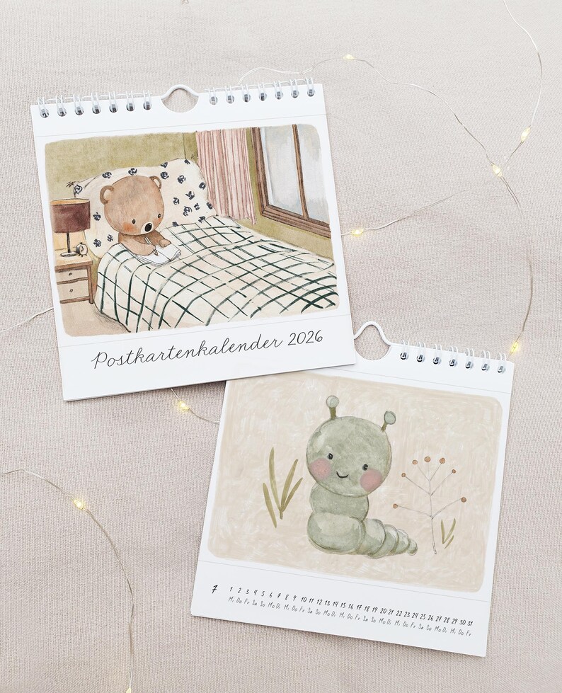 May include: Two spiral-bound calendars with watercolor illustrations. One shows a teddy bear in bed, the other a smiling caterpillar. The text "Postkartenkalender 2026" is on the top calendar. The bottom calendar has a calendar grid.