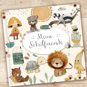 Może przedstawiać: Biała okładka książki z akwarelową ilustracją zwierząt i tytułem "Meine Schulfreunde". Zwierzęta to miś, szop, ż&oacute;łw, lew, banan i dziewczynka w ż&oacute;łtym płaszczu przeciwdeszczowym.