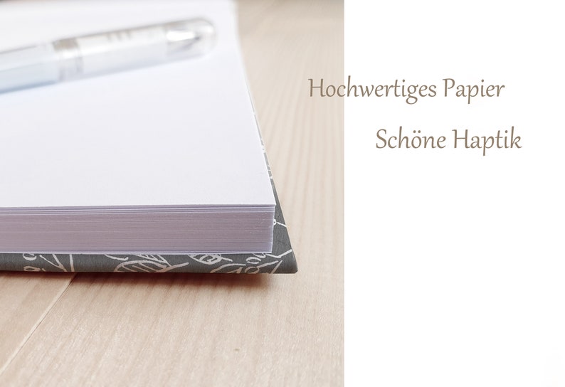 May include: Close-up of a white notebook with a gray and white patterned cover. The notebook is closed and a pen is lying on top of it. The text "Hochwertiges Papier Sch&ouml;ne Haptik" is visible on the right side of the image.