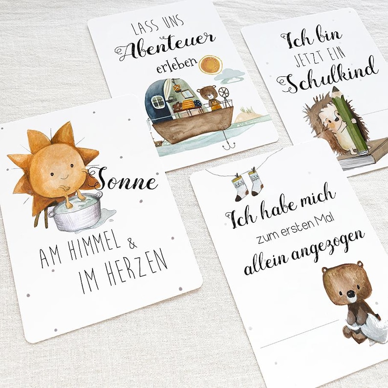 May include: Four illustrated cards with different messages and images. The first card has a sun with a face and the text "Sonne am Himmel & im Herzen". The second card has a boat with a bear and the text "Lass uns Abenteuer erleben". The third card has a hedgehog with a pencil and the text "Ich bin jetzt ein Schulkind". The fourth card has a bear with socks and the text "Ich habe mich zum ersten Mal allein angezogen".