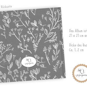 May include: A gray fabric cover with a white floral pattern. The text "Die R&uuml;ckseite" is at the top of the cover. The text "Das Album ist 21 x 21 cm gro&szlig;. Dicke des Buches: Ca. 1, 2 cm" is on the right side of the cover. A white circle with the text "pipapier" is in the center of the cover.