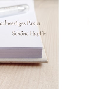 May include: Close-up of the spine of a bound book with white pages. The text on the spine reads "Hochwertiges Papier Sch&ouml;ne Haptik".
