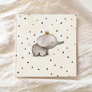May include: A white book cover with a black and white pattern of small triangles. A gray elephant with a yellow crown is in the center of the cover.