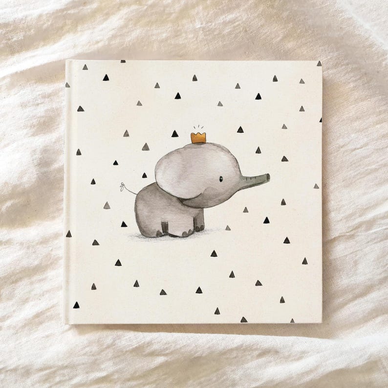 May include: A white book cover with a black and white pattern of small triangles. A gray elephant with a yellow crown is in the center of the cover.