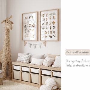 Op de afbeelding: Twee ingelijste dierlijke alfabetposters met een lichtbruine houten lijst, hangend aan een witte muur boven een lichtbruine houten bank met zes opbergbakken. De bank heeft drie lichtbruine kussens met witte en grijze patronen. Een groot geweven giraffen speelgoed staat links van de bank.