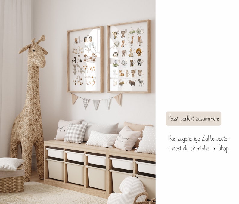 Op de afbeelding: Twee ingelijste dierlijke alfabetposters met een lichtbruine houten lijst, hangend aan een witte muur boven een lichtbruine houten bank met zes opbergbakken. De bank heeft drie lichtbruine kussens met witte en grijze patronen. Een groot geweven giraffen speelgoed staat links van de bank.