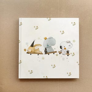 May include: A white book cover with a whimsical illustration of a bunny, an elephant, and a koala riding on toy skateboards. The background is white with a subtle pattern of green leaves.