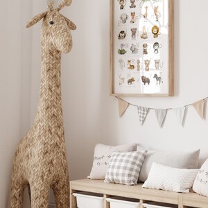 Peut inclure: Une affiche d'alphabet encadr&eacute;e avec des illustrations d'animaux de A &agrave; Z. L'affiche est accroch&eacute;e &agrave; un mur blanc au-dessus d'un banc en bois avec des coussins. Un grand jouet en forme de girafe tiss&eacute; se tient dans le coin de la pi&egrave;ce.