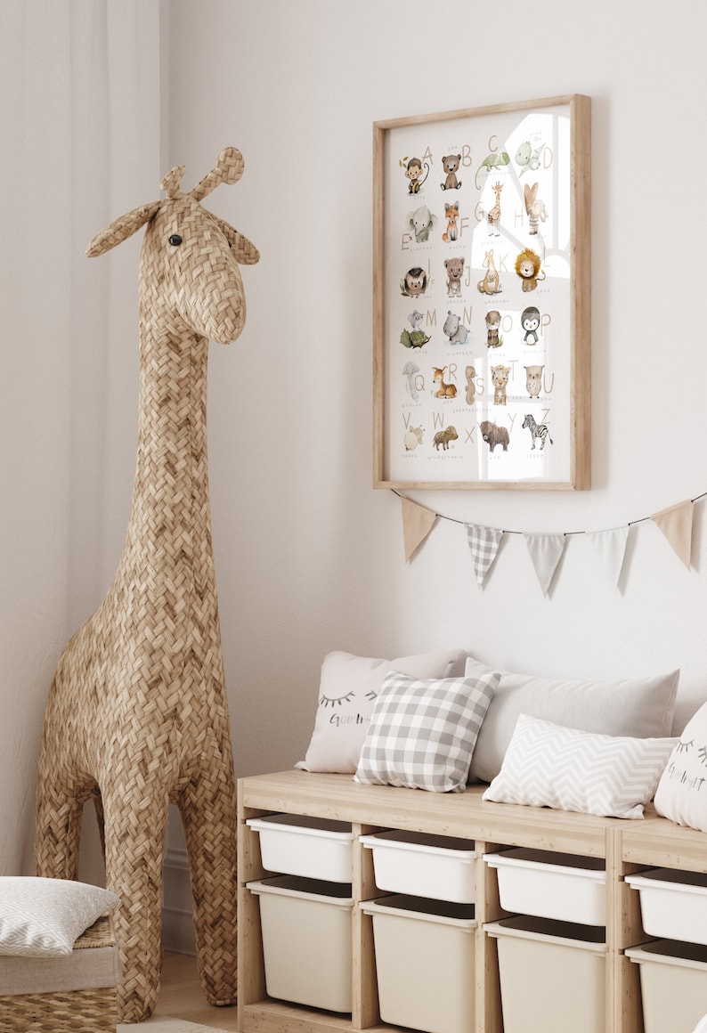 Peut inclure: Une affiche d'alphabet encadr&eacute;e avec des illustrations d'animaux de A &agrave; Z. L'affiche est accroch&eacute;e &agrave; un mur blanc au-dessus d'un banc en bois avec des coussins. Un grand jouet en forme de girafe tiss&eacute; se tient dans le coin de la pi&egrave;ce.