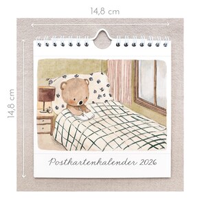 May include: A spiral-bound calendar featuring a watercolor illustration of a teddy bear writing in a notebook on a bed. The calendar is 14.8 cm (5.8 inches) square and has the text "Postkartenkalender 2026" at the bottom.