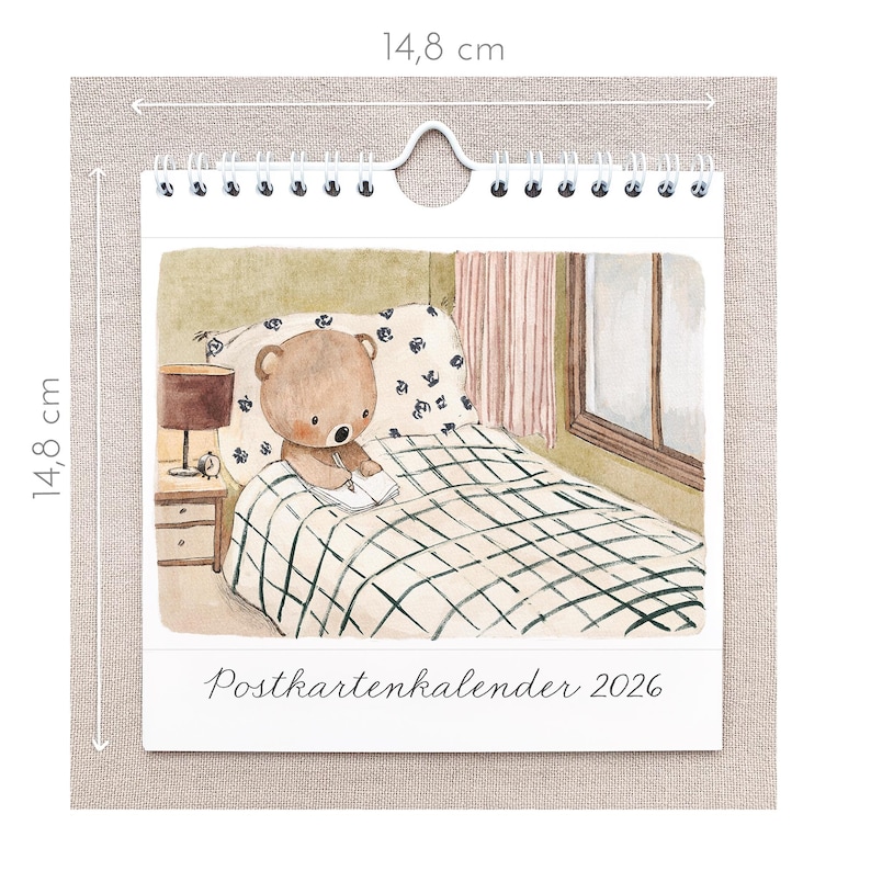 May include: A spiral-bound calendar featuring a watercolor illustration of a teddy bear writing in a notebook on a bed. The calendar is 14.8 cm (5.8 inches) square and has the text "Postkartenkalender 2026" at the bottom.