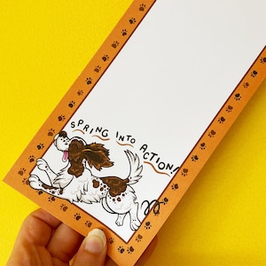 May include: A brown and white dog with a paw print border on a white card with the text "Spring into action!" printed on it.