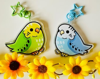 Può includere: Due portachiavi a forma di pappagallo cartoon colorati con ciondoli a forma di stella. I pappagalli sono verdi e blu con accenti bianchi. I portachiavi sono appesi a un ramo di girasoli gialli.