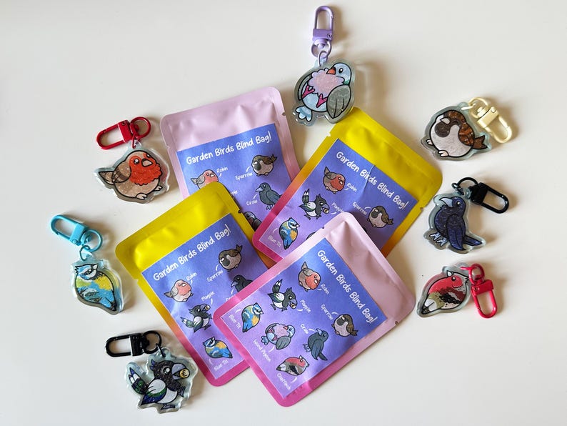 May include: A set of eight colorful keychains featuring different types of birds. Each keychain has a clear plastic charm with a cartoon bird illustration and the text "Garden Birds Blind Bag!" printed on the packaging.