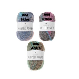 Può includere: Tre gomitoli di lana in diverse combinazioni di colori. La lana è etichettata "Painted Power" e ha i numeri di colore 004 Skies, 005 Ethno e 006 Aqua.