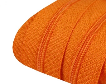 May include: Close-up of a vibrant orange zipper. The zipper teeth and tape are clearly visible, showcasing the texture and construction. The bright color suggests use in clothing or accessories, adding a pop of color to any project.