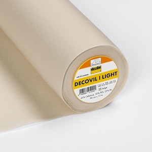 Peut inclure: Un rouleau de tissu d'entoilage beige Decovil I Light. L'étiquette indique "Decovil I Light", "beige", "43% Cellulose, 30% PES, 25% PA", "90 cm x 1,5 m" et comprend des instructions de lavage.
