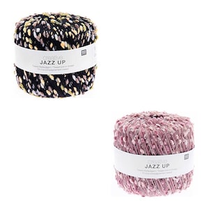 Könnte beinhalten: Zwei Knäuel Garn, eines schwarz mit mehrfarbigen Flecken und eines rosa. Beide Knäuel haben den Text "creative JAZZ UP" und "Tweed Belugam/Tweed knit-in thread" auf dem Etikett.