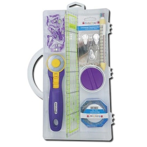 Può includere: Un kit da cucito contenente un taglierino rotante viola e giallo, un righello trasparente con segni verdi, clip viola, un cerchio viola, spilli e un contenitore blu e bianco di spilli. Il kit è confezionato in una custodia di plastica trasparente con manico bianco.