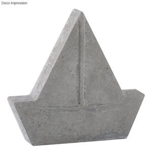 Könnte beinhalten: Eine graue Betonskulptur eines Segelboots. Die Skulptur ist so gestaltet, dass sie wie ein einfaches Segelboot mit einem einzigen Segel aussieht.