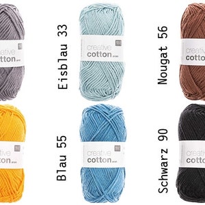 Può includere: Assortimento di gomitoli di filato in vari colori, tra cui giallo, arancione, blu, grigio, marrone e nero. Ogni gomitolo ha un'etichetta bianca con il testo "creative cotton..." stampato su di essa.