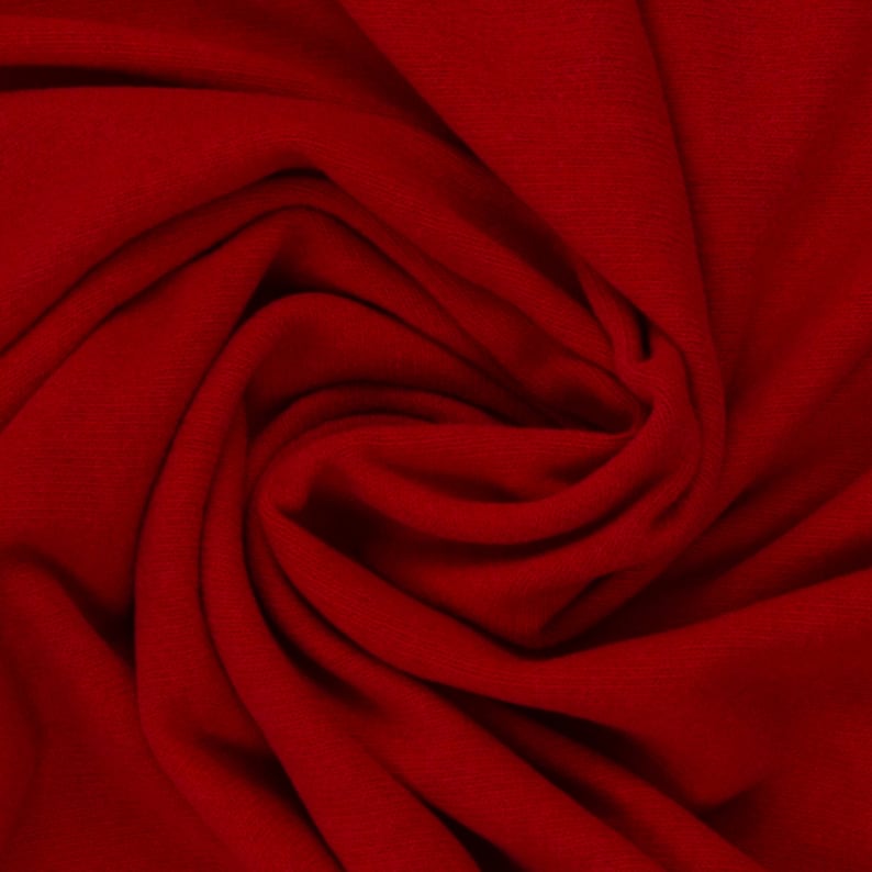 Puede incluir: Primer plano de una tela de color rojo intenso con una superficie suave y texturizada. La tela est&aacute; doblada y drapeada, creando un patr&oacute;n de remolino.