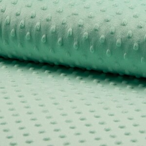 May include: A close-up of a soft, mint green fabric with a textured, dotted pattern. The fabric is folded in half, showing the texture of the dots.