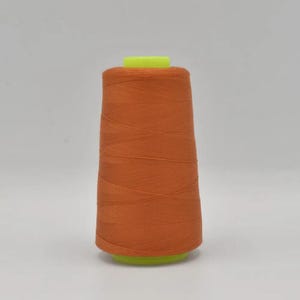 Könnte beinhalten: Eine Spule mit orangefarbenem Garn, das auf einer Kunststoffspule gewickelt ist.