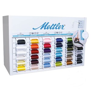 May include: A white display stand with a variety of spools of thread in different colours. The spools are labelled with the brand name "Mettler" and the text "SERAFLEX".