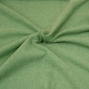 Könnte beinhalten: Nahaufnahme eines weichen, grünen Stoffes mit einer strukturierten Oberfläche. Der Stoff ist gefaltet und drapiert, wodurch seine Textur und sein Fall sichtbar werden.