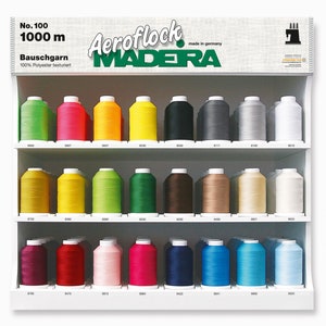 Può includere: Un espositore di bobine di filo di poliestere testurizzato Aeroflock Madera da 1000 metri in vari colori. Le bobine sono disposte su tre ripiani. Il testo "No. 100 1000 m Bauschgarn 100% Polyester texturiert" è visibile nella parte superiore dell'espositore.