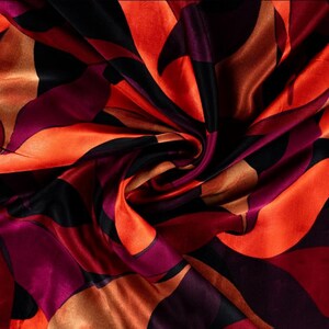 Könnte beinhalten: Nahaufnahme eines Seidenstoffs mit abstraktem Design. Der Stoff weist ein wirbelndes Muster aus orangefarbenen, schwarzen und burgunderfarbenen Formen auf. Der Stoff hat eine glänzende, glatte Textur, und die Farben verschmelzen zu einem dynamischen visuellen Effekt.
