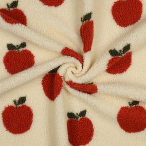 Könnte beinhalten: Ein cremefarbener Sherpa-Fleece-Stoff mit einem sich wiederholenden Muster aus strukturierten roten Äpfeln mit dunkelgrünen Stielen und Blättern. Das Material hat eine dicke, flauschige und weiche Florstruktur mit einem wirbelnden Fall.