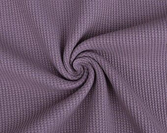 May include: A close-up of a soft, textured fabric in a muted purple colour. The fabric is woven in a waffle pattern, creating a raised, textured surface.