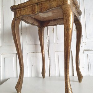 May include: A small, antique gold-painted table with a scalloped edge and four curved legs. The table has a distressed finish, revealing hints of the underlying wood. The table is a decorative accent piece.