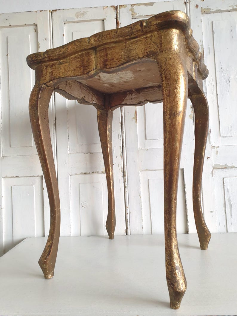 May include: A small, antique gold-painted table with a scalloped edge and four curved legs. The table has a distressed finish, revealing hints of the underlying wood. The table is a decorative accent piece.