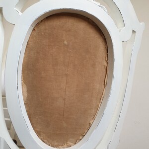 Puede incluir: Silla blanca pintada con respaldo tallado y asiento de tela marr&oacute;n.