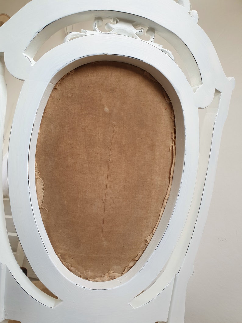 Puede incluir: Silla blanca pintada con respaldo tallado y asiento de tela marr&oacute;n.