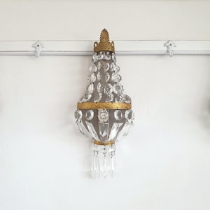 Puede incluir: Tres apliques de pared ornamentados con detalles de cristal y dorado. Los apliques tienen forma de l&aacute;grima, con cristales transparentes que caen de una corona dorada. Est&aacute;n montados en una pared blanca.