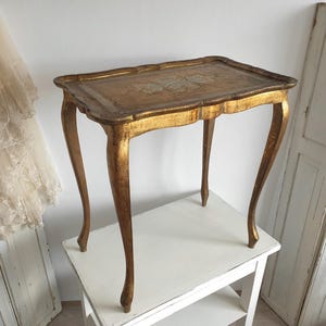 May include: An antique-style side table, painted gold, with a rectangular top and curved legs. The table's surface has a decorative design. The table measures approximately 71 cm long, 46 cm wide, and 66 cm tall.