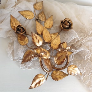 May include: Gold metal wall decor featuring a bouquet of roses with leaves. The roses are stylized and have a vintage look.