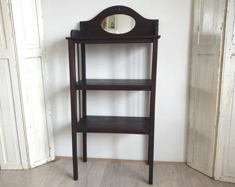 Op de afbeelding: Een donkerbruin houten rek met drie planken en een decoratieve bovenkant. De bovenkant heeft een ovale spiegel en gesneden details. Het rek is vrijstaand en heeft een eenvoudig, elegant ontwerp.