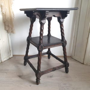 May include: Dark brown antique side table with a square top and a lower shelf. The table features intricately carved details and twisted legs. The table is approximately 28 inches tall.