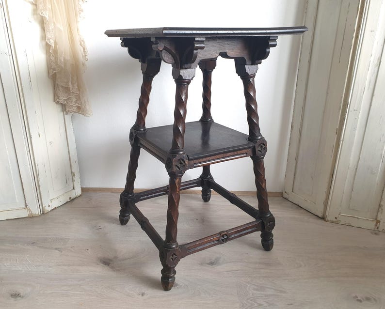 May include: Dark brown antique side table with a square top and a lower shelf. The table features intricately carved details and twisted legs. The table is approximately 28 inches tall.